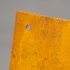 Nahaufnahme von der Ecke eines Cortenstahlschildes. Man sieht die rostige Oberfläche im Detail sowie kleine stellen, wo das silberne Stahl am Rand durchschaut.