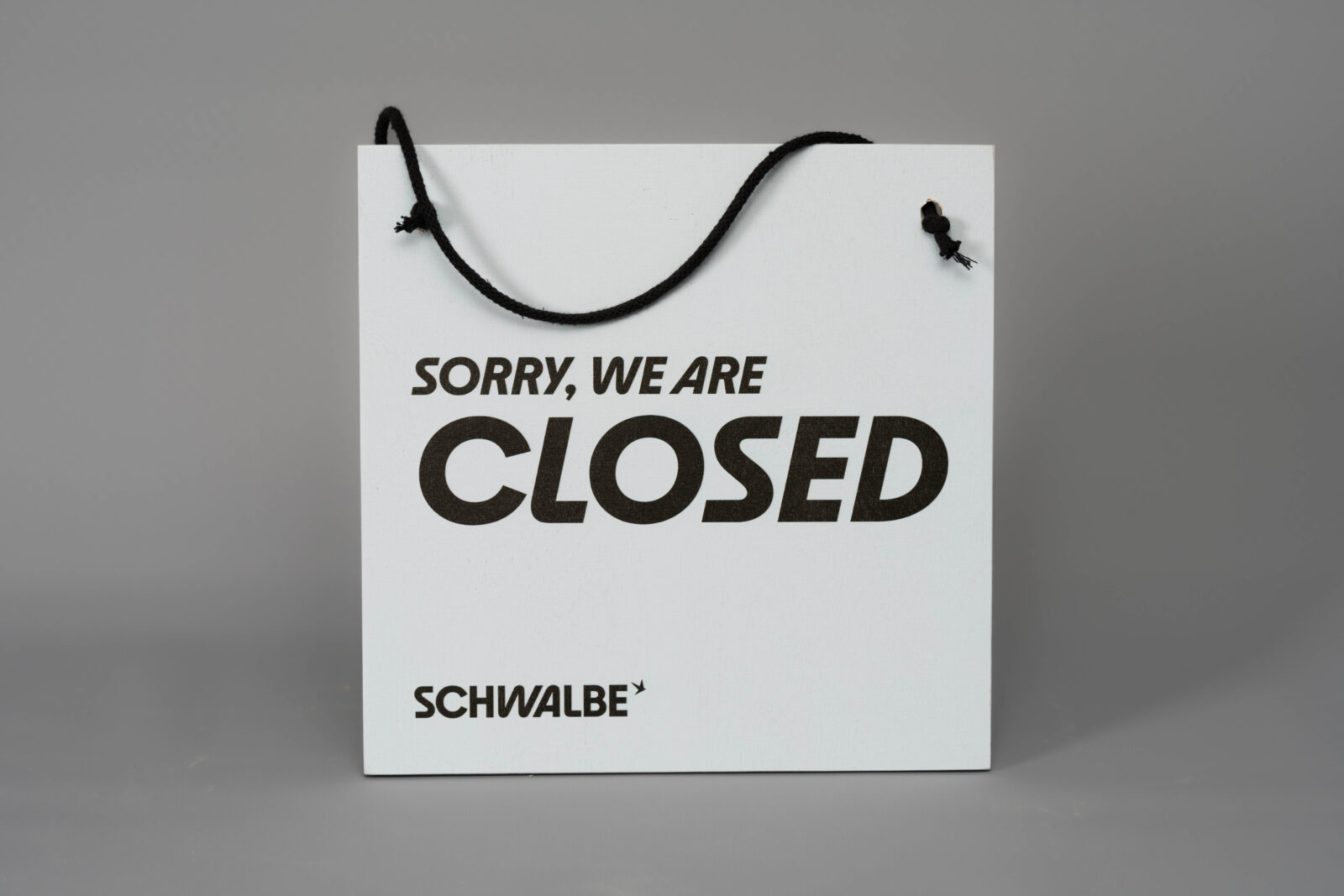 Bedrucktes Multiplex-Schild mit dem Text "SORRY, WE ARE CLOSED" in schwarz auf hellblauem Hintergrund, Aufhängeseil ist durch zwei Löcher gefädelt und geknotet.
