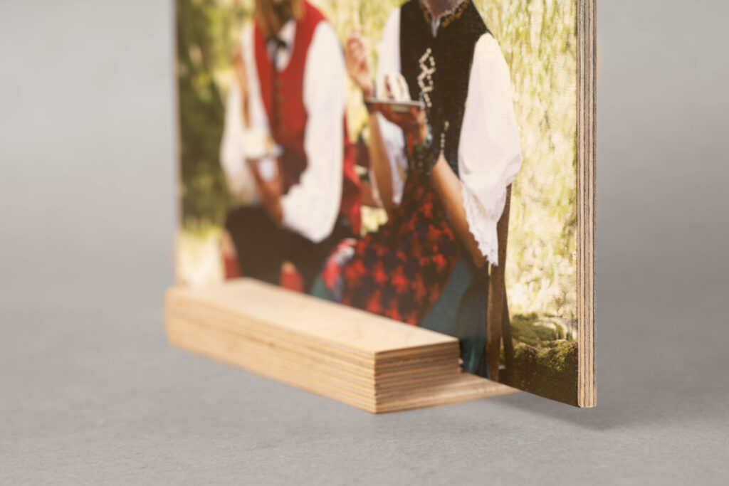 Schild auf Multiplex-Holz gedruckt wird auf seinem Holz-Sockel vor einem grauen Hintergrund gezeigt. Die Nahaufnahme von der Seite zeigt die Schichten des Multiplex-Holzes.