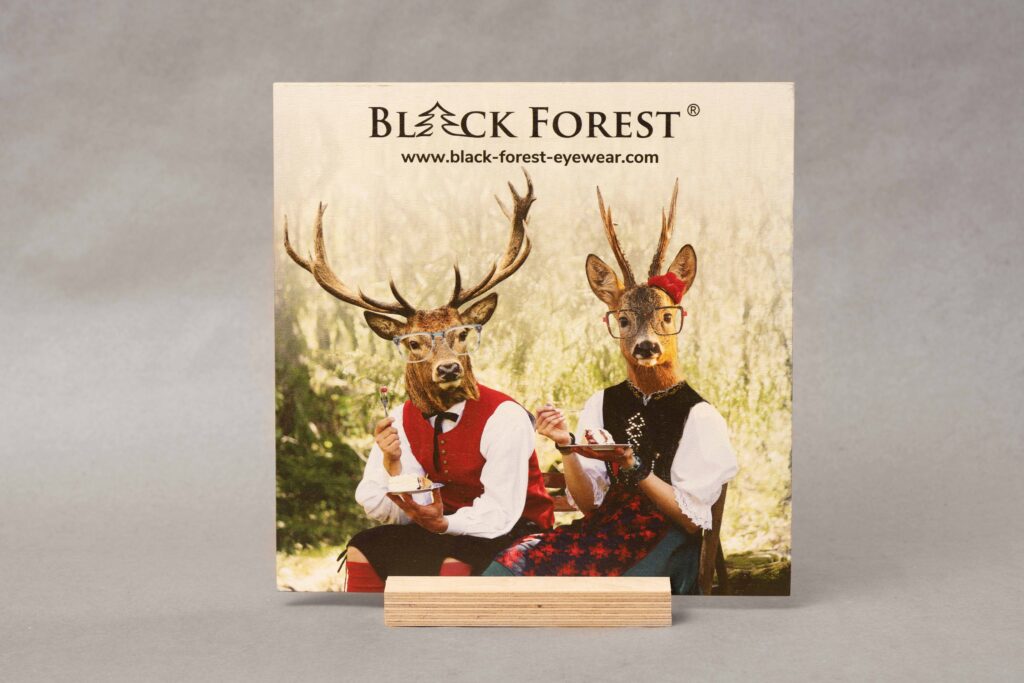 Werbe-Schild gedruckt auf Multiplex-Holz. Steht auf einem Holzsockel vor einem grauen Hintergrund.