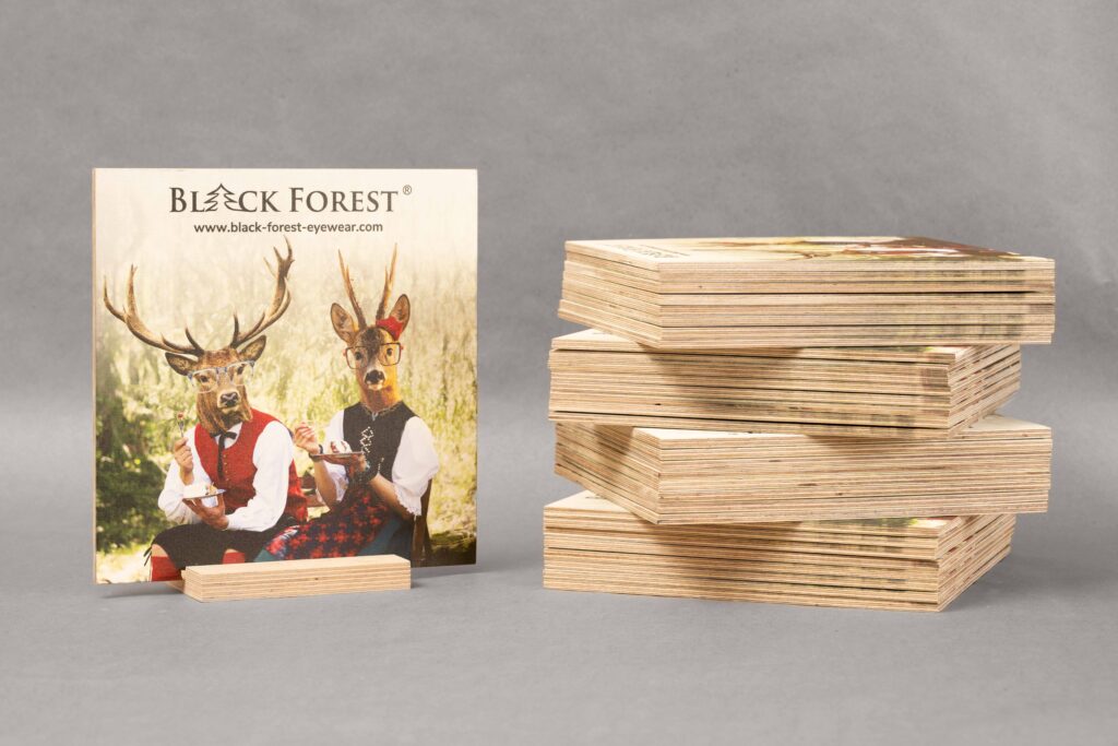 Multiplex Werbe-Schild auf einem Holzsockel vor einem grauen Hintergrund. Ein Stapel von weiteren Schildern steht neben dran.