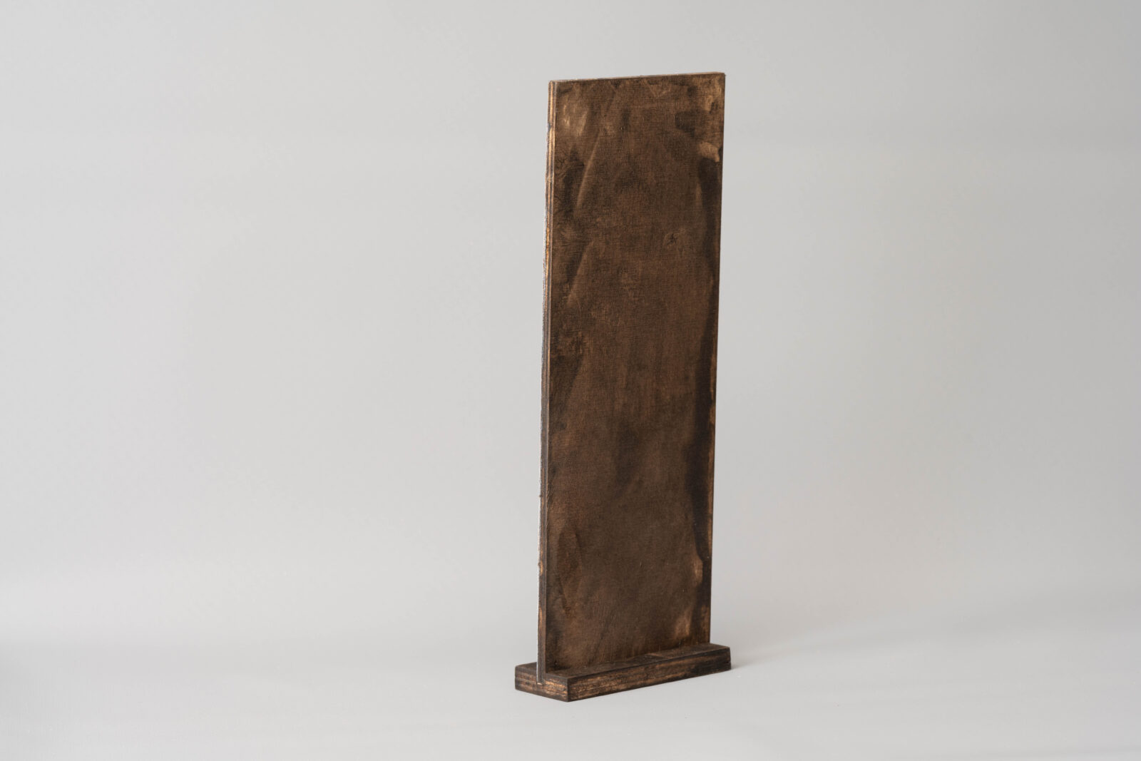 Dunkel gebeizte Rückseite eines stehenden Multiplex-Schildes auf Holzsockel. Geziegt im leichten Winkel auf grauem Hintergrund.